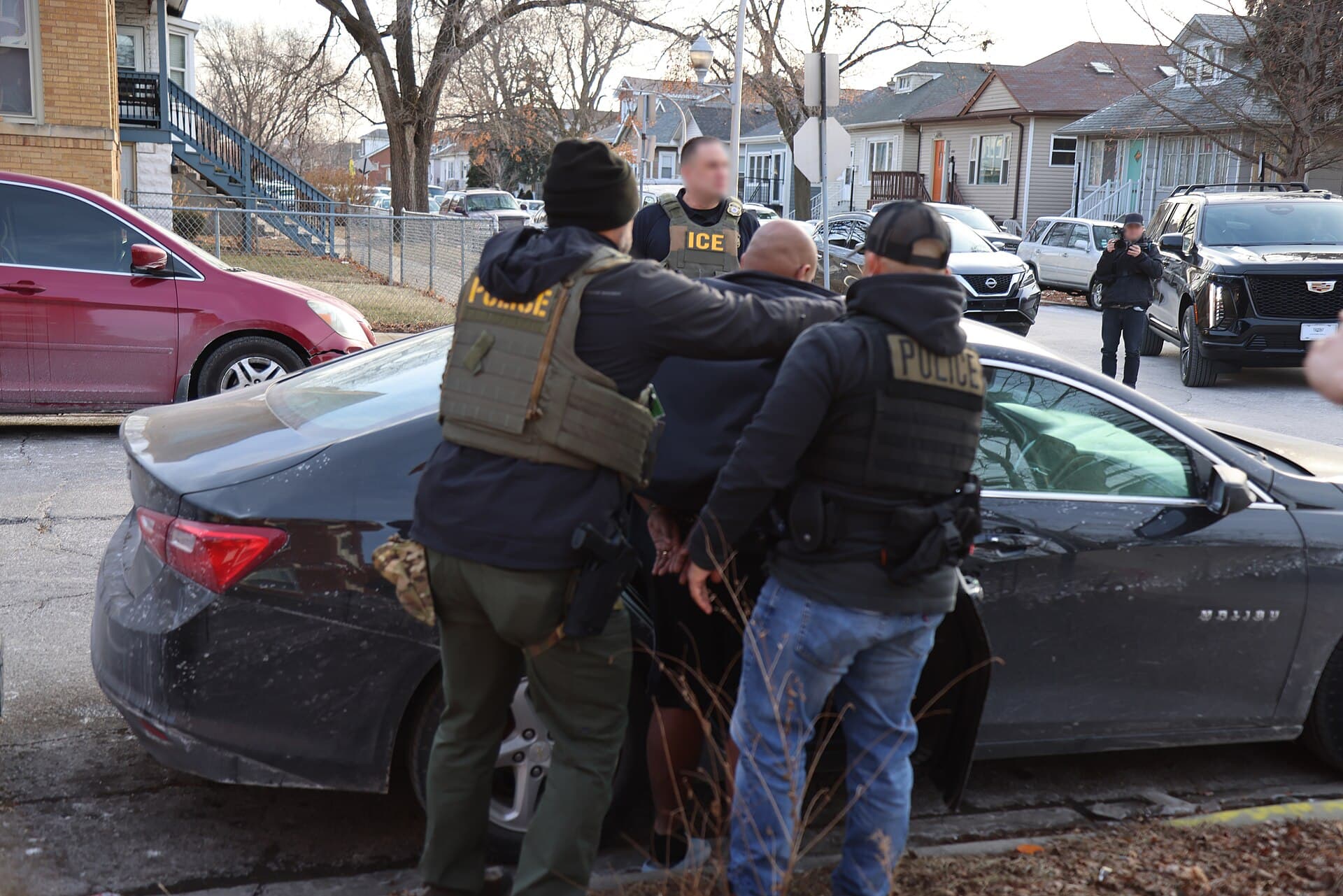 ICE and federal officers detain a man beside a car on a residential street in Chicago